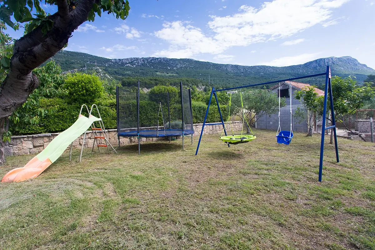 Private outdoor children's playground in the garden of the house, equipped with swings, a slide, and a trampoline.